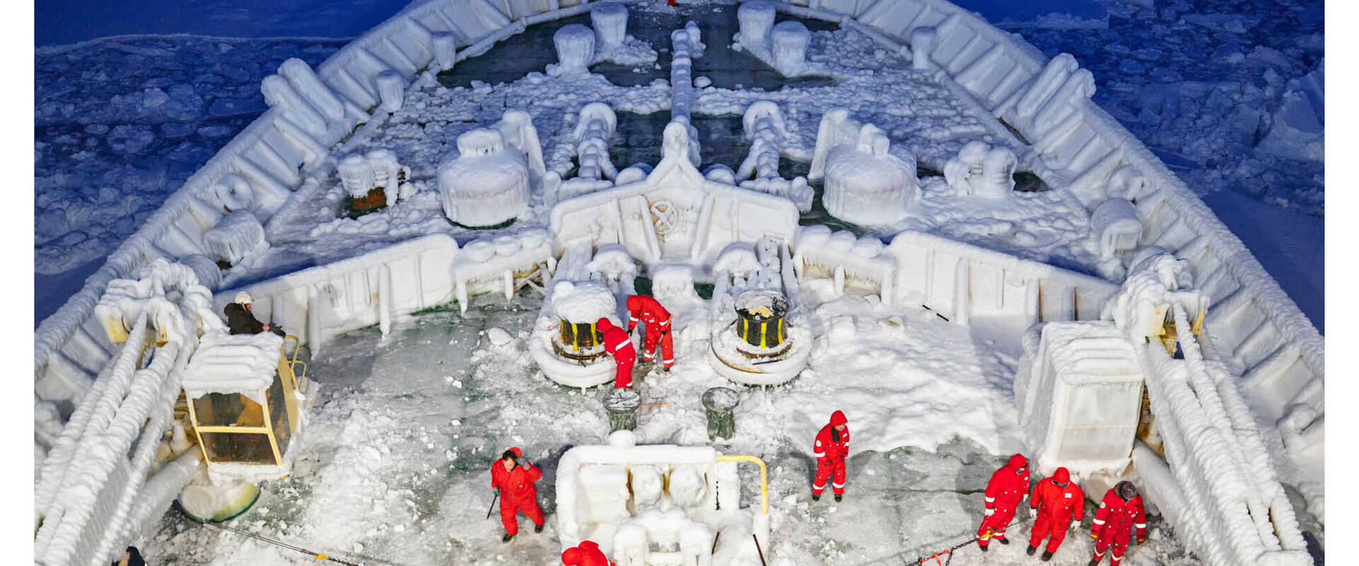 Der Vorderteil eines mit Eisschicht &uuml;berzogenen Schiffes, auf dem Wissenschaftler in Schutzanz&uuml;gen arbeiten.